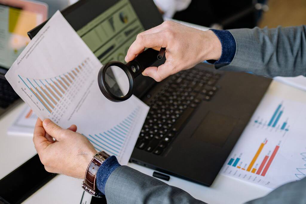 A business owner analyzing charts with a magnifying glass.